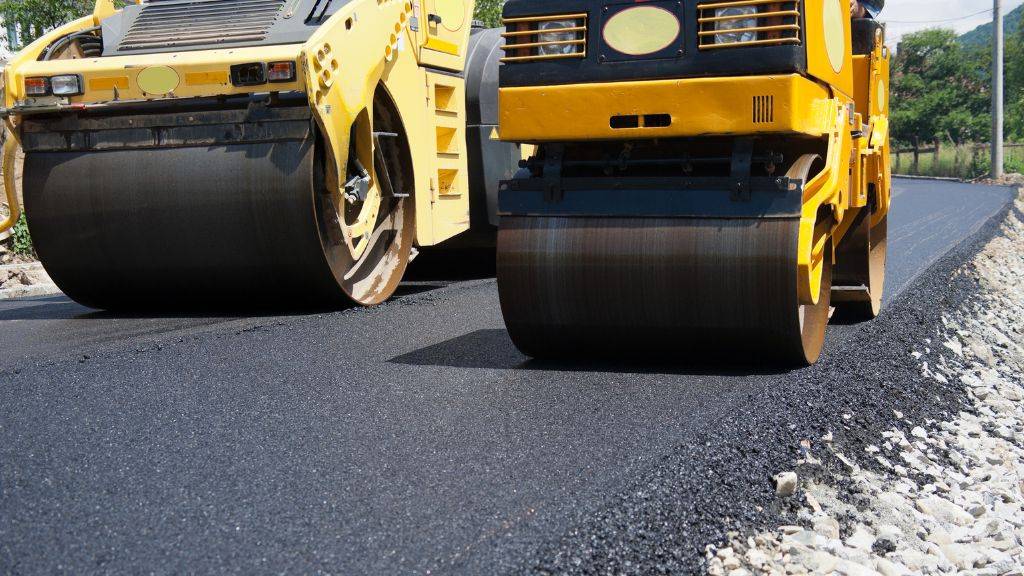 Heavy compaction rollers smoothing hot-mix asphalt during a summer driveway paving project in Heath and Rockwall TX