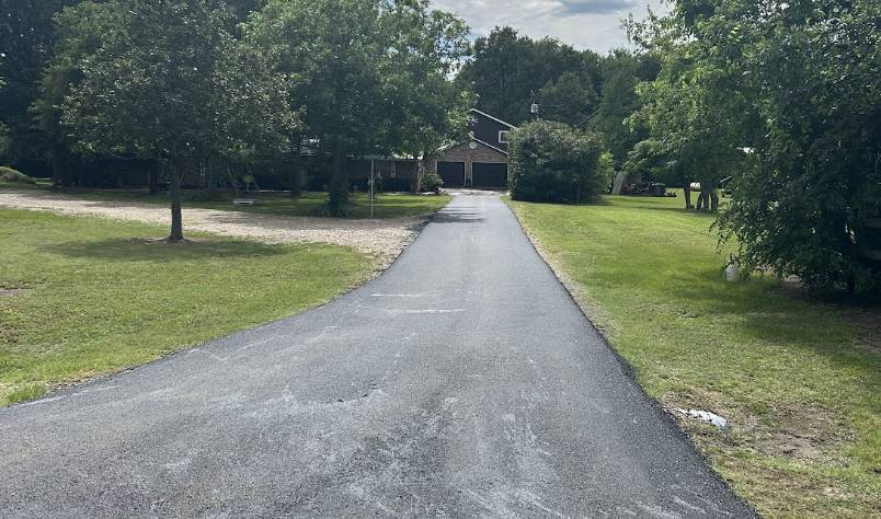Long freshly paved asphalt driveway leading to a residential home surrounded by green lawn and trees in Heath TX by Gentry's Paving Group