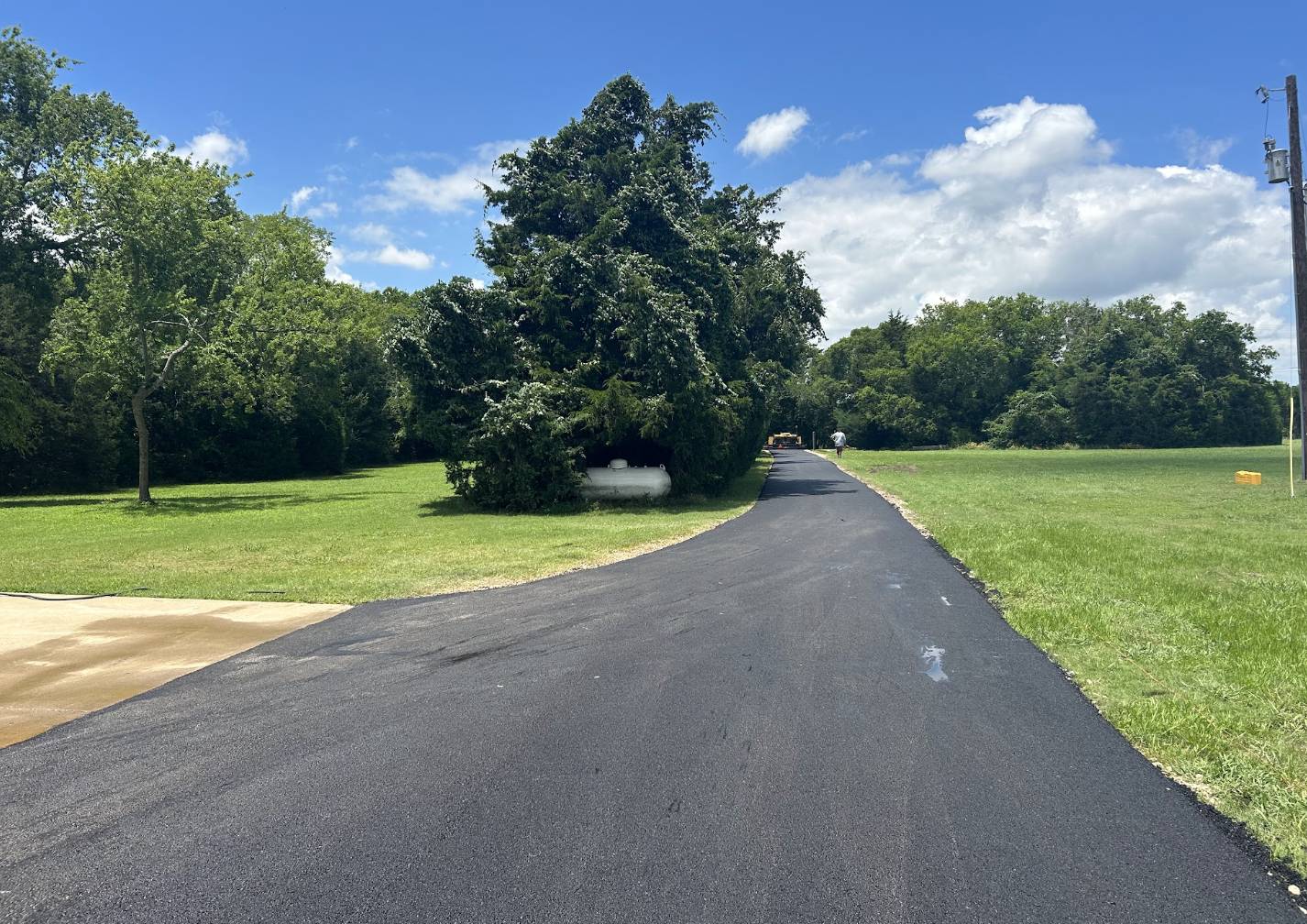 Long smooth asphalt driveway extending through a grassy rural property in Rockwall TX paved by Gentry's Paving Group.