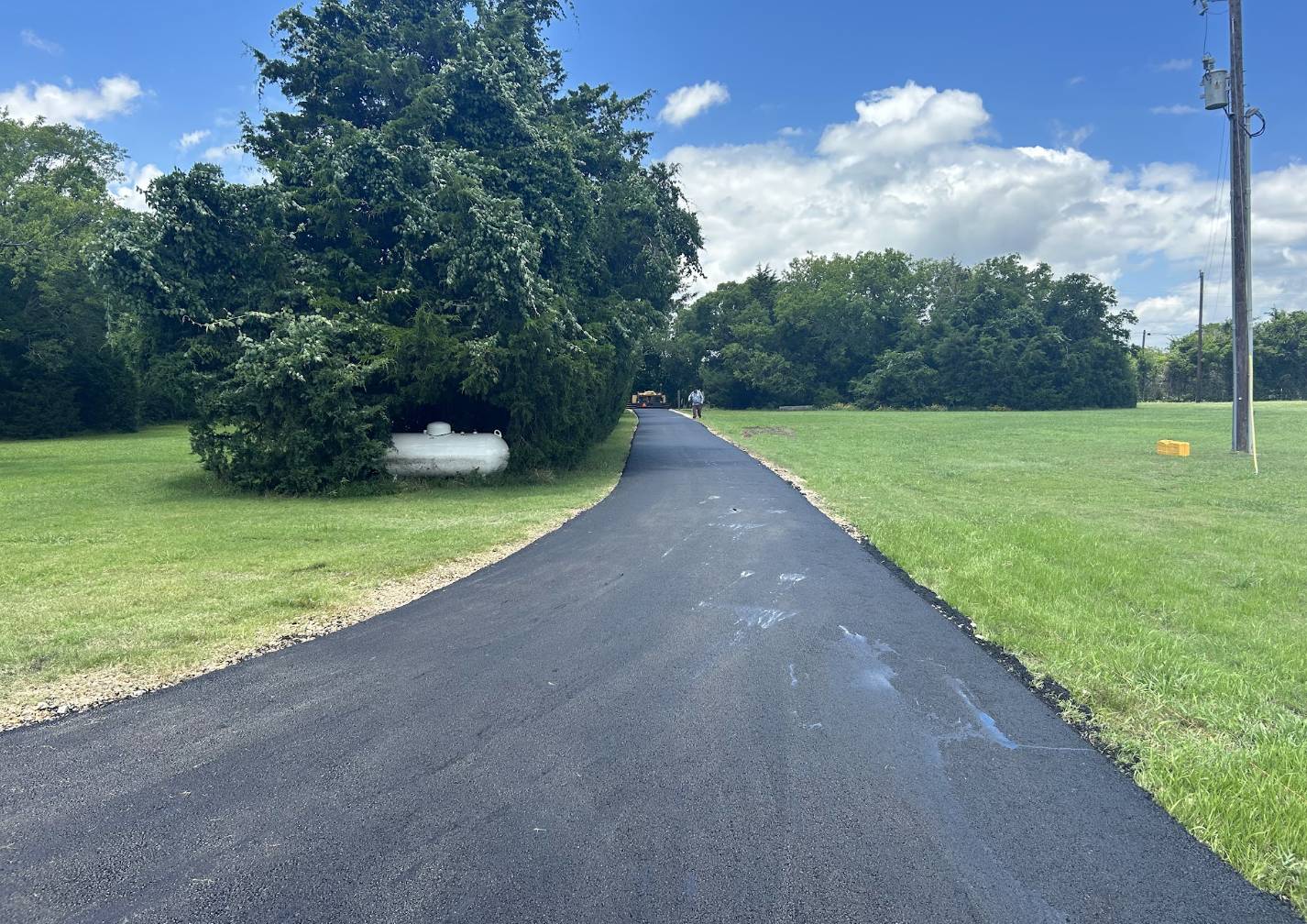 Smooth long asphalt driveway extending through open green fields on a rural property in Rowlett TX paved by Gentry's Paving Group.