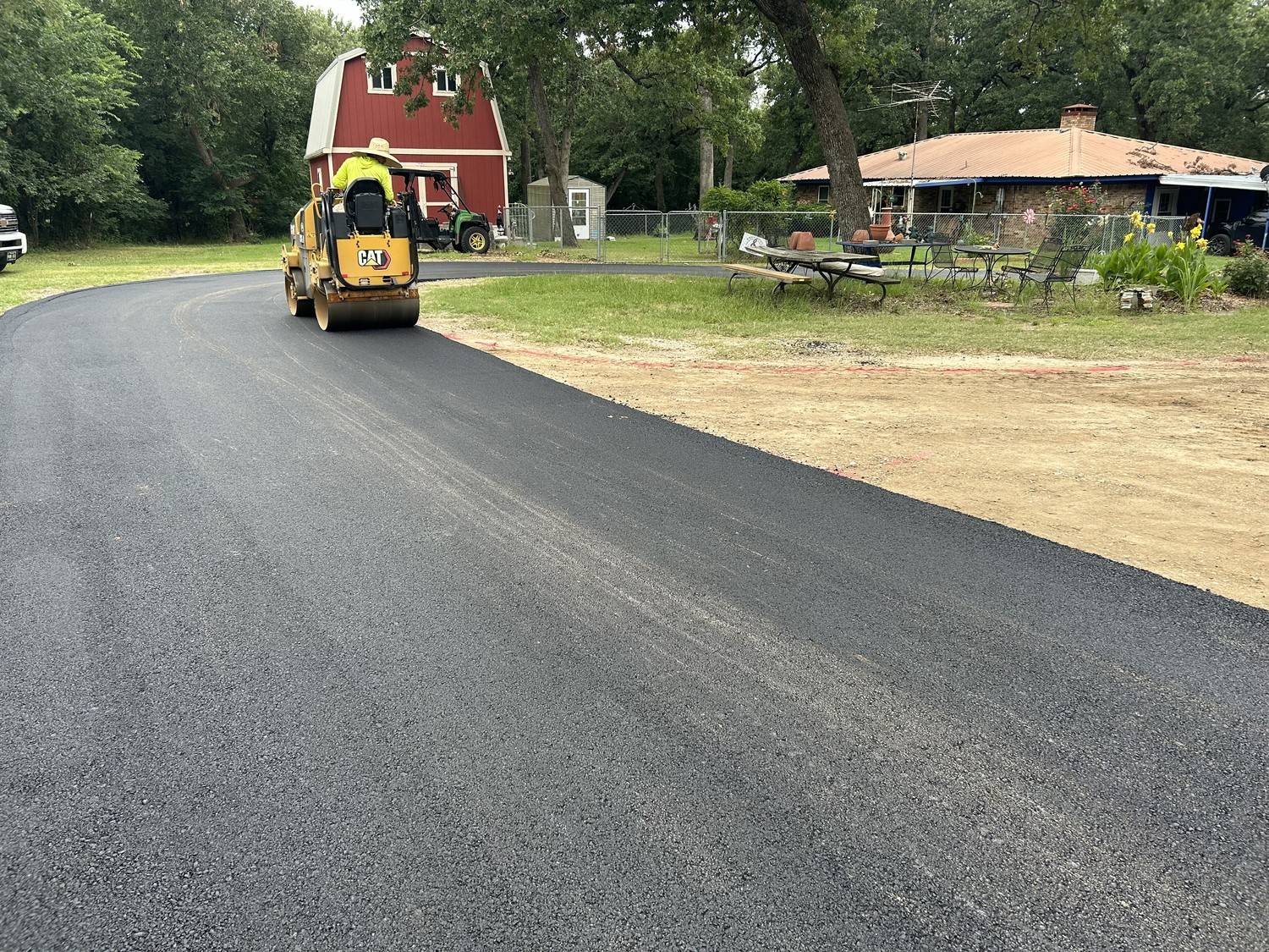 Yellow CAT roller compacting a fresh asphalt curved residential driveway on a rural property in Fate TX by Gentry's Paving Group.