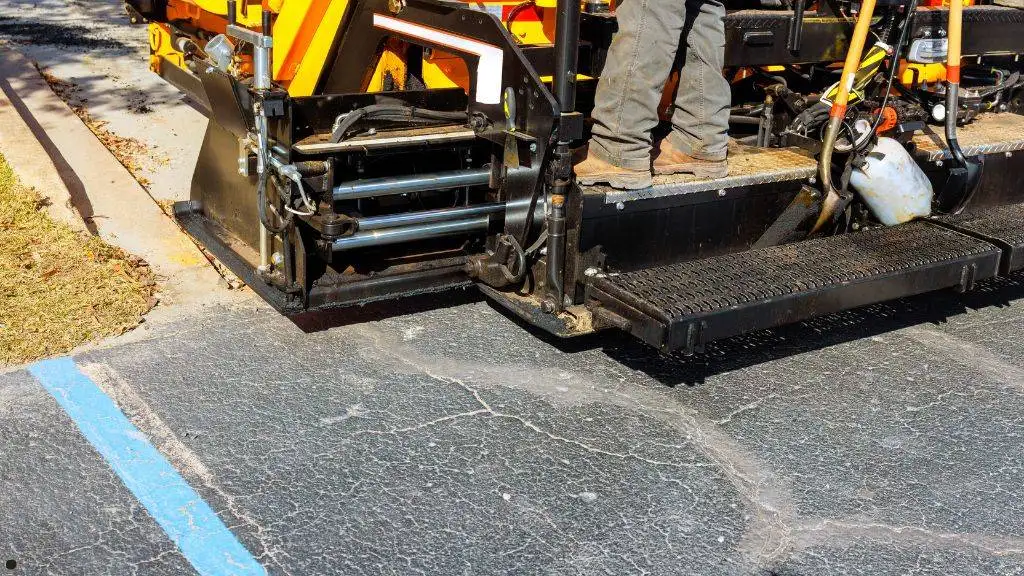 Heavy paving equipment screed preparing to lay fresh asphalt overlay on cracked parking lot pavement in DFW.