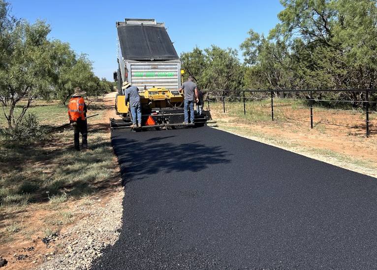 Paving equipment laying hot asphalt for a long rural driveway on a property in Forney TX by Gentry's Paving Group.