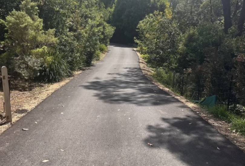 Long smooth blacktop driveway running through a wooded rural property in Royse City TX.