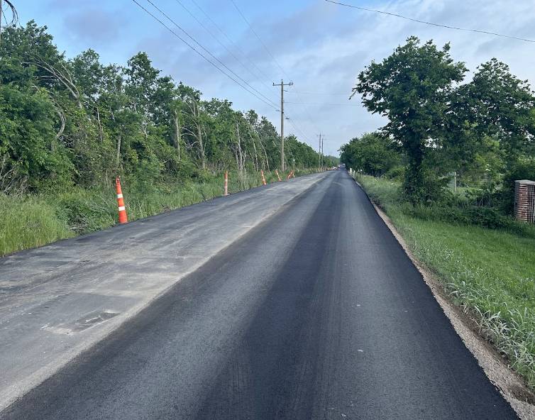 Newly resurfaced blacktop rural road stretching through green countryside in Talty TX.